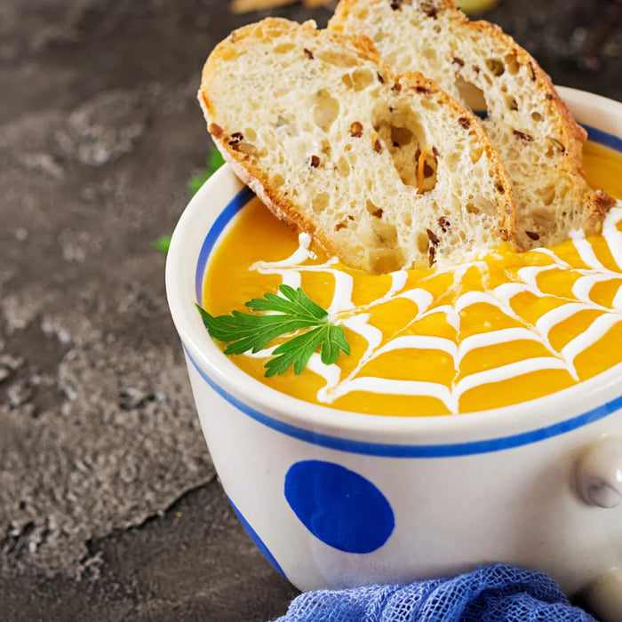 Soupe de citrouille d’Halloween décorée en toile d’araignée avec crème, servie avec tranches de pain grillé et persil frais