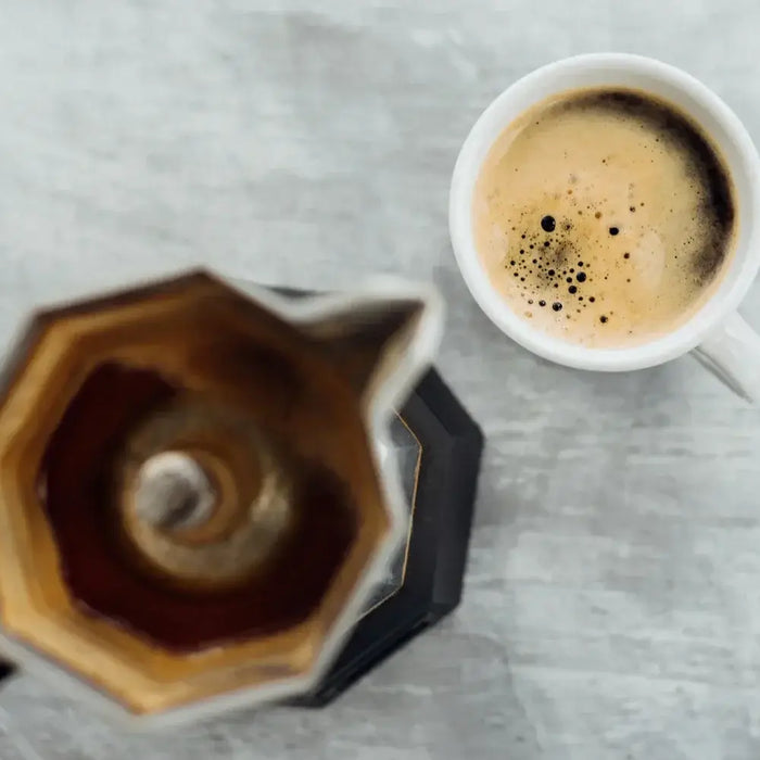 Vue du dessus d’une cafetière italienne moka et d’une tasse de café crémeux sur une table claire — le rituel du café à l’italienne.