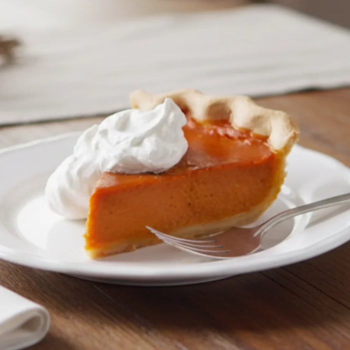 Tarte à la citrouille américaine servie sur une assiette blanche, garnie de crème fouettée, posée sur une table en bois — dessert crémeux et parfumé à la cannelle, typique d’Halloween et de Thanksgiving.