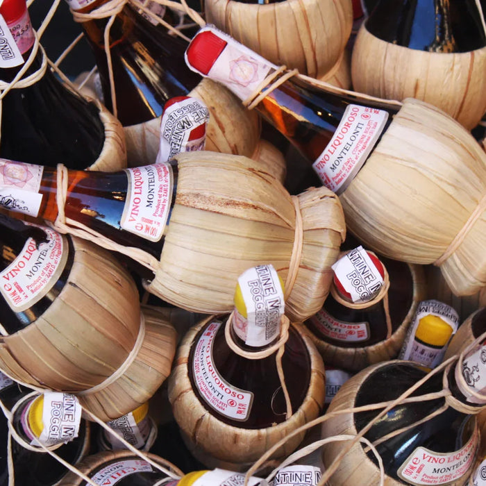 Bouteilles traditionnelles de vin Chianti enveloppées de paille dans un panier, symbolisant l’artisanat et l’authenticité des vins toscans.