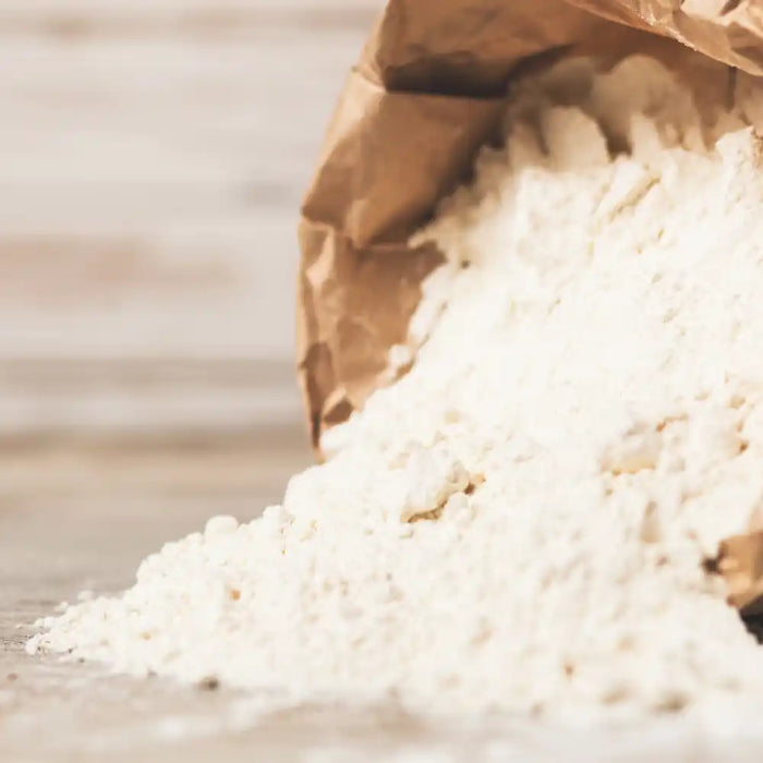 Farine italienne type 00 versée d’un sac en papier sur un plan de travail, idéale pour pizzas et pâtes fraîches.