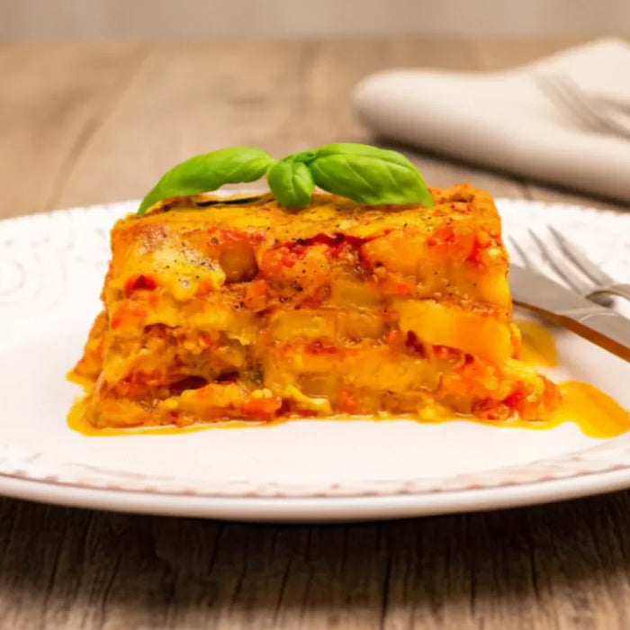 Parmigiana de courge servie chaude sur assiette blanche, gratinée à la sauce tomate, au parmesan et garnie de basilic frais