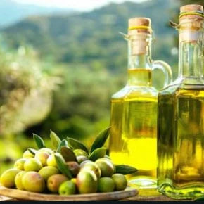Deux bouteilles d’huile d’olive italienne artisanale et un plateau d’olives fraîches sur une table en plein air, avec un paysage méditerranéen en arrière-plan — EasyGusto.fr