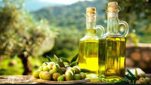 Deux bouteilles d’huile d’olive italienne artisanale et un plateau d’olives fraîches sur une table en plein air, avec un paysage méditerranéen en arrière-plan — EasyGusto.fr